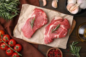 Fresh raw meat with rosemary, tomatoes and spices on wooden table, flat lay